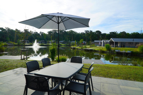 Terrasse mit Tisch und Sonnenschirm am Seeufer der Velthorst-Lodge in Zilverstrand, Belgien.