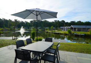 Terraza con mesa y sombrilla junto al lago en la cabaña Velthorst en Zilverstrand, Bélgica.