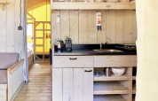 Keuken in de safari tent Villatent Outback met houten kasten, wasbak, waterkoker en zicht op de slaapkamer.