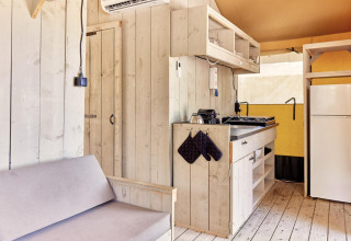 Vista interna della tenda safari Villatent Outback con pareti in legno chiaro, cucina e frigorifero.