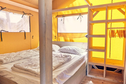 Binnenkant van een Villatent Outback safaritent met dubbel bed, houten rekken, kapstokken en ramen.