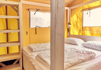 Innenraum eines Villatent Outback Safari-Zelts mit Doppelbett, Holzregalen und gelben Zeltwänden.