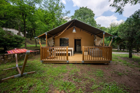 Tienda safari Villatent Nomad con terraza de madera en Camping La Clémentine, Francia, rodeada de árboles.