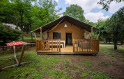 Tienda safari Villatent Nomad con terraza de madera en Camping La Clémentine, Francia, rodeada de árboles.