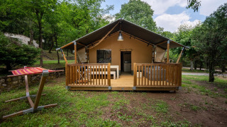 Safaritent Villatent Nomad met houten veranda op Camping La Clémentine in Frankrijk, tussen de bomen.