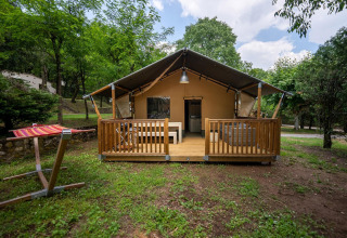 Safaritent Villatent Nomad met houten terras op Camping La Clémentine in Frankrijk, omgeven door bomen.