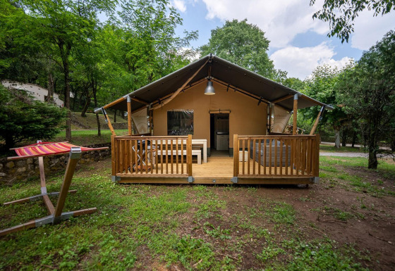 Safaritent Villatent Nomad met houten veranda op Camping La Clémentine in Frankrijk, tussen de bomen.