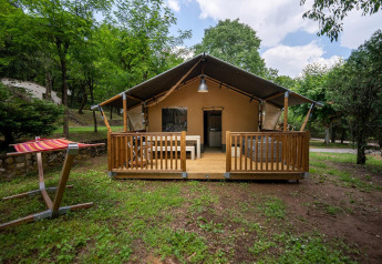 Tienda safari Villatent Nomad con terraza de madera en Camping La Clémentine, Francia, rodeada de árboles.