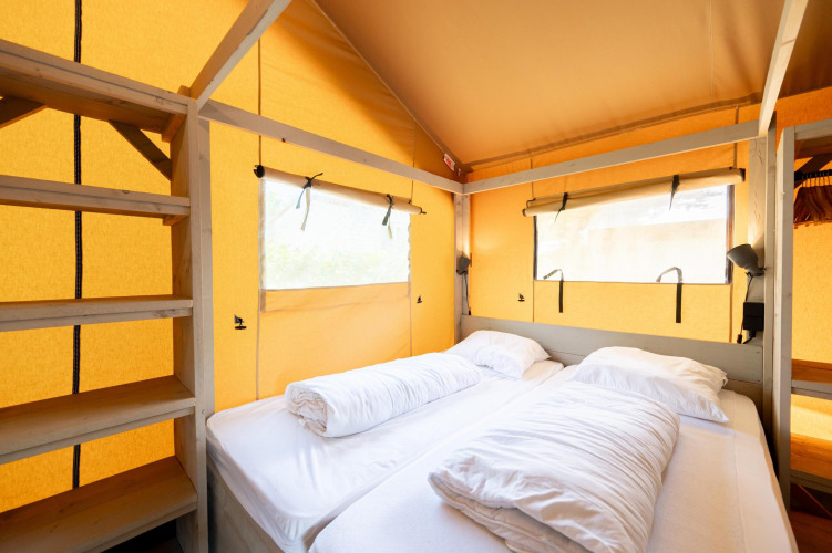 Interior de una tienda safari Villatent Nomad con cómodas camas y estantes en Camping La Clémentine, Francia.