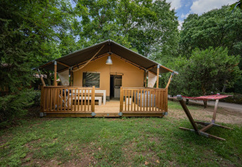 Tienda safari Villatent Nomad con terraza de madera y hamaca en Camping La Clémentine rodeada de árboles.