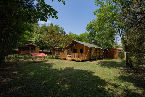 Tienda safari Villatent Nomad en Camping La Clémentine, Francia, rodeada de naturaleza y una hamaca roja.