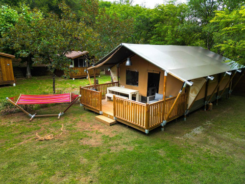 Safari tent Villatent Nomad met veranda en hangmat op Camping La Clémentine in Frankrijk, omgeven door bomen.