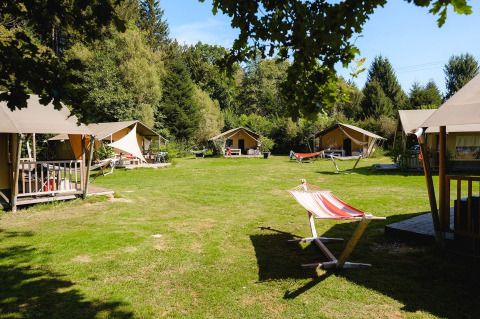 Tiendas safari y hamacas sobre césped en Villatent Wood, Camping Au Clos de La Chaume, Francia.