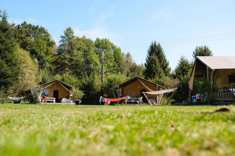 Tres tiendas safari con hamacas en un camping verde en Au Clos de La Chaume, Francia, rodeadas de bosque.