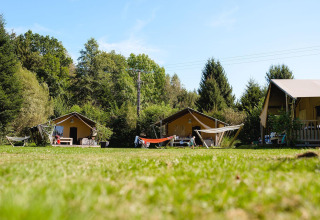 Tre tende safari con amache su un prato verde al campeggio Au Clos de La Chaume, circondato da alberi.