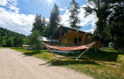 Tienda safari Villatent Wood en Camping de Vaubarlet, Francia, rodeada de árboles y hamacas bajo el sol.