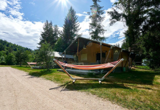 Tienda safari Villatent Wood en Camping de Vaubarlet, Francia, rodeada de árboles y hamacas bajo el sol.