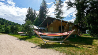 Tente safari Villatent Wood au Camping de Vaubarlet en France avec hamacs et arbres, sous un ciel ensoleillé.