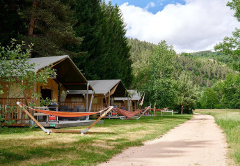 Safaritenten met hangmatten bij Camping de Vaubarlet in Frankrijk, tussen bomen en groene heuvels.
