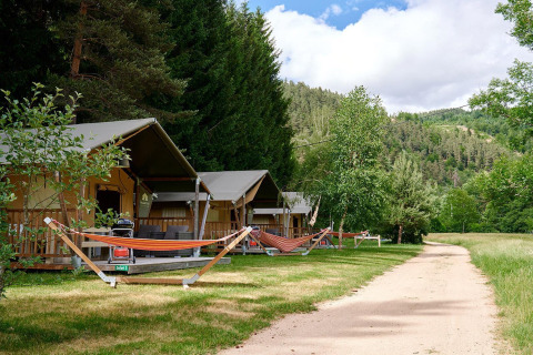 Tentes safari avec hamacs au Camping de Vaubarlet en France, entourées de verdure et de collines boisées.