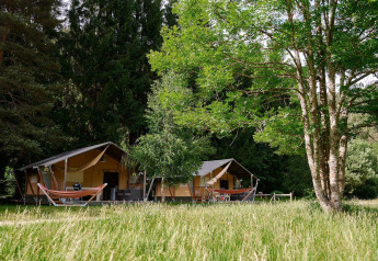 Villatent Wood safaritenten bij Camping de Vaubarlet in Frankrijk, omgeven door groen en hoge bomen.
