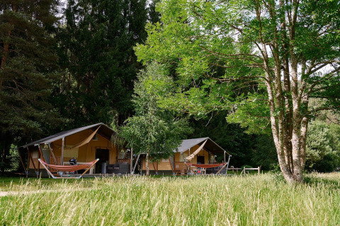 Villatent Wood safaritenten bij Camping de Vaubarlet in Frankrijk, omgeven door groen en hoge bomen.