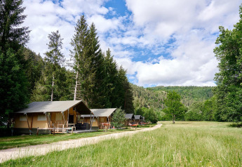 Safari tents at Camping de Vaubarlet in France, surrounded by forest, grass, and a bright sky.