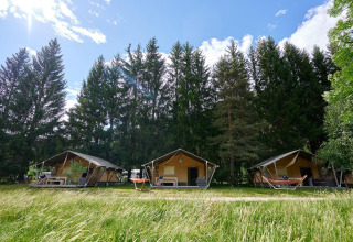 Safari tenten bij Camping de Vaubarlet in Frankrijk, omgeven door groene bomen en gras onder een blauwe lucht.