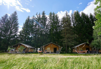 Safari tenten bij Camping de Vaubarlet in Frankrijk, omgeven door groene bomen en gras onder een blauwe lucht.