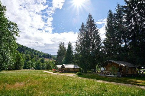Area campeggio soleggiata con tenda safari Villatent Wood al Camping de Vaubarlet, circondata dal verde.