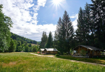 Safari-Zelt Villatent Wood auf Camping de Vaubarlet in Frankreich, sonnige Wiese mit hohen Bäumen.
