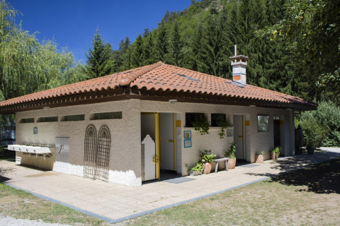 Edificio sanitario con techo de tejas rojas en Camping de Vaubarlet, Francia, rodeado de bosque verde.