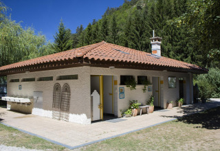 Edificio sanitario con techo de tejas rojas en Camping de Vaubarlet, Francia, rodeado de bosque verde.
