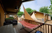Tienda safari Villatent Outback en Camping La Masia, España, con hamaca y terraza rodeada de árboles frondosos.