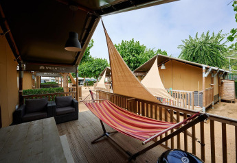 Tenda safari Villatent Outback al Camping La Masia in Spagna con amaca e veranda tra verde e altri alloggi.