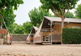 Safaritent Villatent Outback bij Camping La Masia in Spanje, omgeven door groen en grote schaduwrijke bomen.