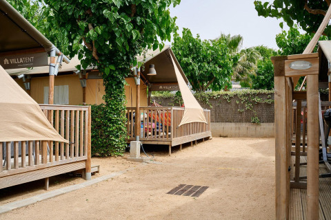 Safari-Zelte von Villatent Outback mit Holzterrassen, Bäumen und sandigem Untergrund auf dem Campingplatz.