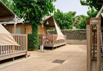 Tiendas safari Villatent Outback con terrazas de madera y árboles, situadas en un tranquilo camping arenoso.