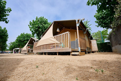 Safari tent Villatent Outback bij Camping La Masia in Spanje, omgeven door bomen en een zanderige ondergrond.