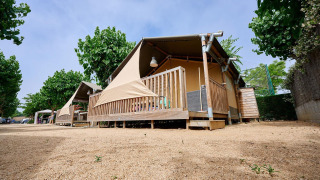 Safari tent Villatent Outback bij Camping La Masia in Spanje, omgeven door bomen en een zanderige ondergrond.