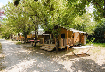 File di lodge Villatent Outback al Medrose Camping in Francia, circondate da alberi verdi e ombreggiati.