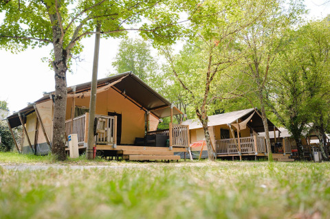 Lodges Villatent Outback en Medrose Camping en Francia, rodeados de árboles verdes y naturaleza tranquila.