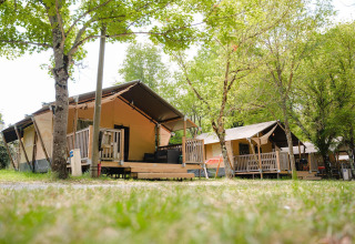 Villatent Outback lodges op Medrose Camping in Frankrijk, omgeven door bomen en een groene omgeving.