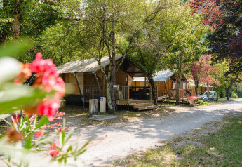 Villatent Outback-lodges bij Medrose Camping in Frankrijk, omgeven door bomen en fleurige zomerbloemen.