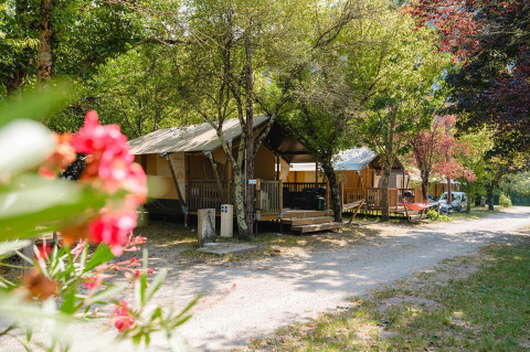 Lodges Villatent Outback al campeggio Medrose in Francia, immersi tra alberi e fiori estivi colorati.