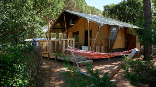 Tienda safari Villatent Outback en Camping Leï Suves, Francia, con terraza de madera y hamaca exterior.