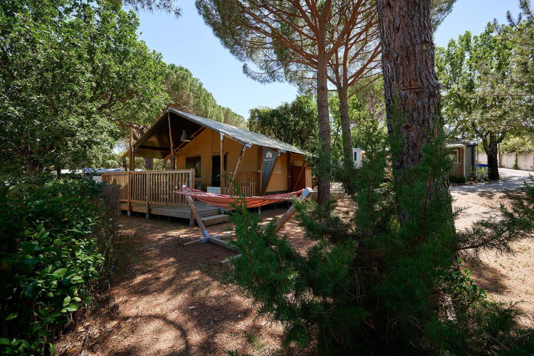 Tienda safari Villatent Outback en Camping Leï Suves en Francia, rodeada de árboles y una hamaca.