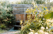 Houten buitenjacuzzi omringd door groene planten en bomen, gefotografeerd bij een sfeervolle lodge.