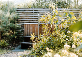 Houten buitenjacuzzi tussen groen bij een gezellig lodge, gefotografeerd op een zonnige dag.