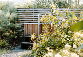 A wooden outdoor hot tub surrounded by lush greenery and trees, photographed at a welcoming lodge.
